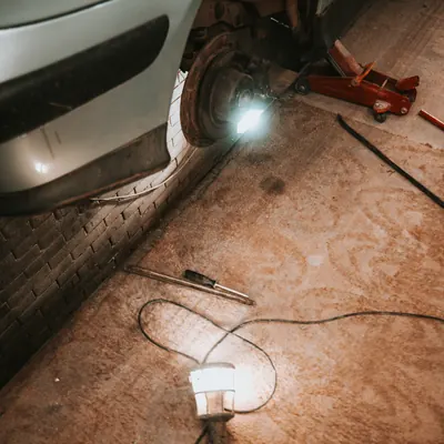 Mașină fără o roată, sprijinită într-un atelier, cu o lampă pe jos